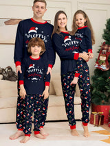 Family of four wearing matching navy blue Merry Christmas pajamas with red trim and festive printed pants beside a Christmas tree.