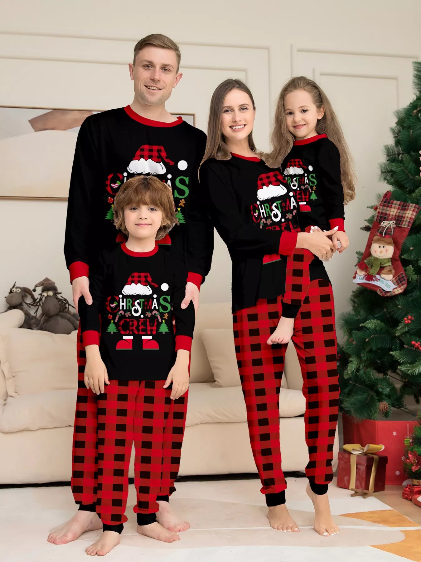 Family of four wearing matching black Christmas Crew pajama tops with red cuffs and red and black buffalo plaid pants beside a Christmas tree.