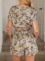 Woman wearing a floral romper in Apricot standing in a room with a neutral background.
