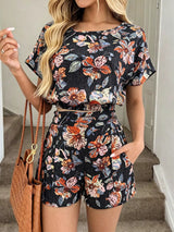 Woman wearing a floral romper with a brown handbag indoors.