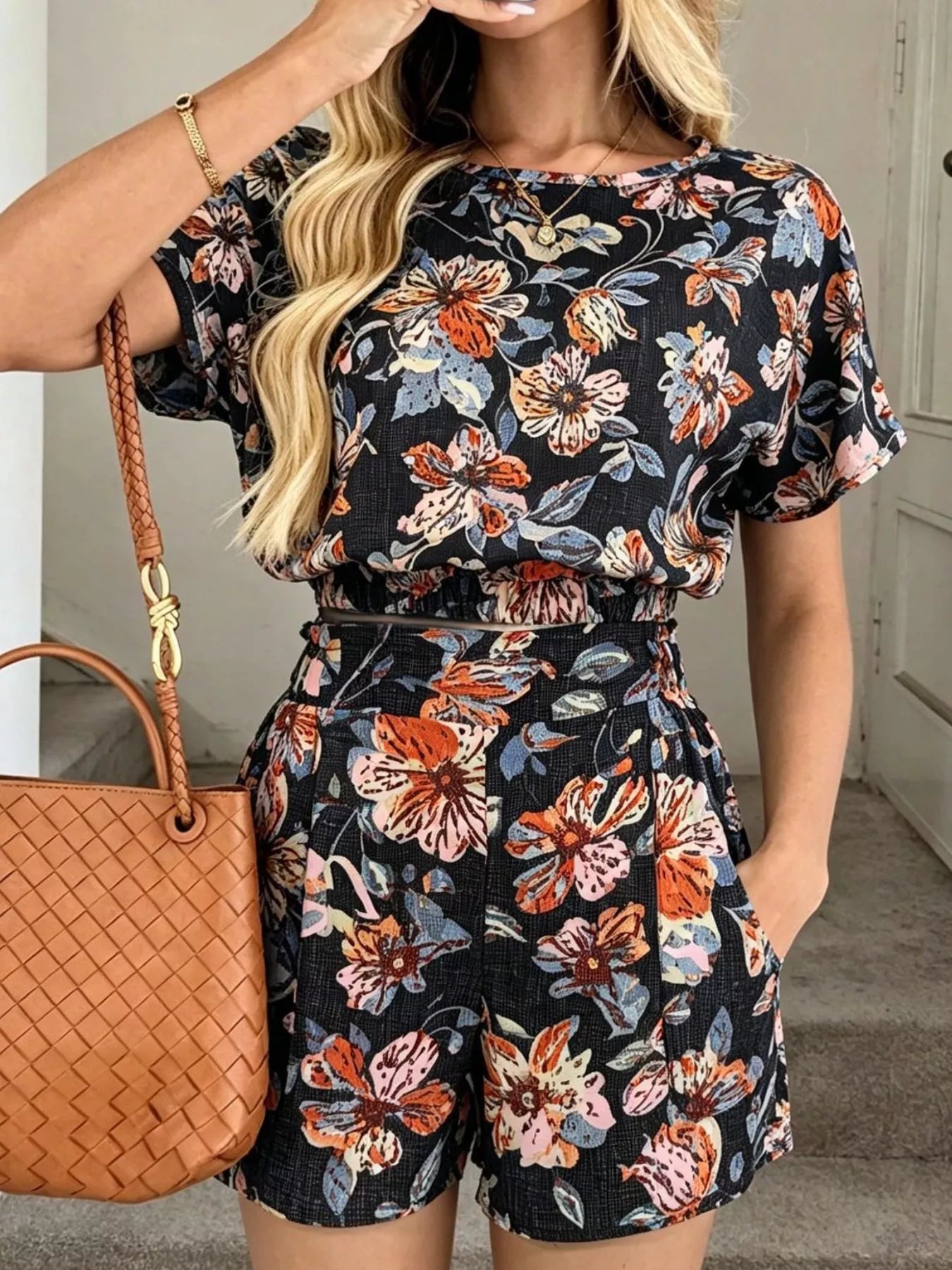 Woman wearing a floral romper with a brown handbag indoors.