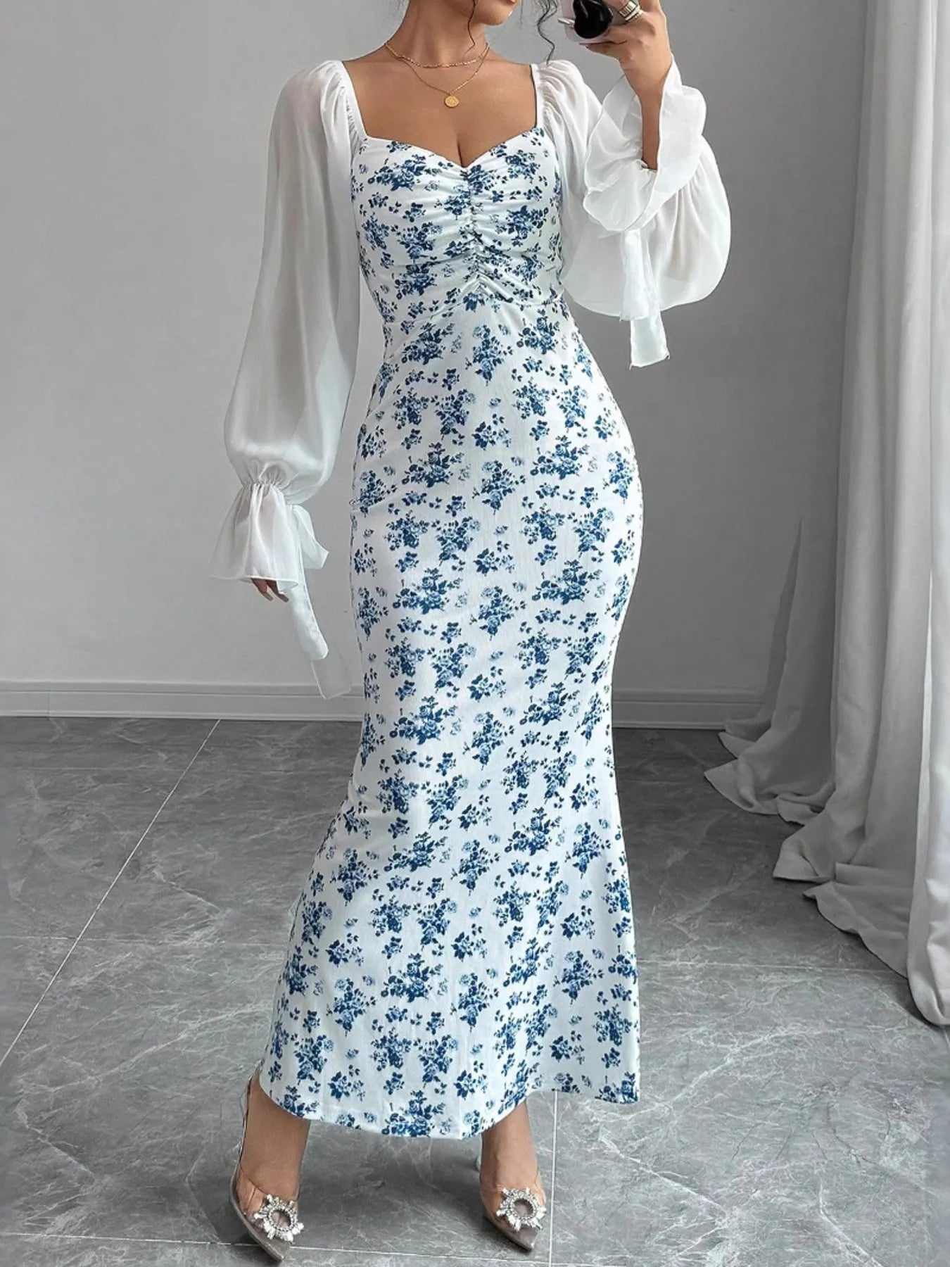 Woman wearing a floral dress with sheer sleeves in an indoor setting