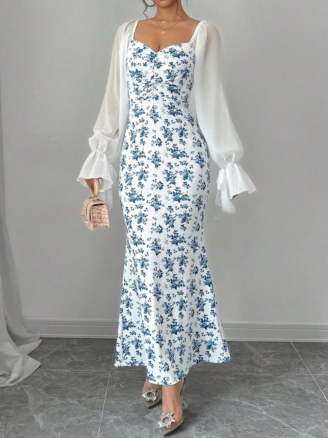 Woman wearing a floral dress with a white sheer sleeves against a gray background