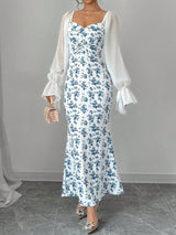 Woman wearing a floral dress with a white sheer sleeves against a gray background