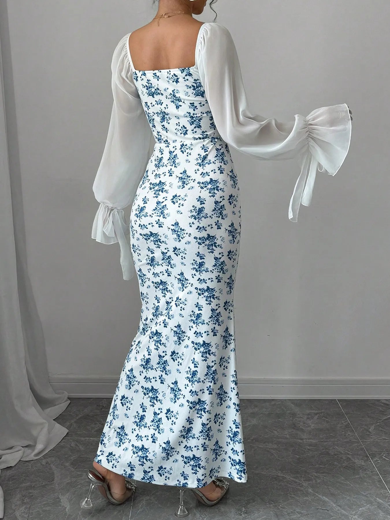 Woman wearing a floral dress with sheer sleeves against a gray background showing the back of the dress.