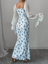 Woman wearing a floral dress with sheer sleeves against a gray background showing the back of the dress.
