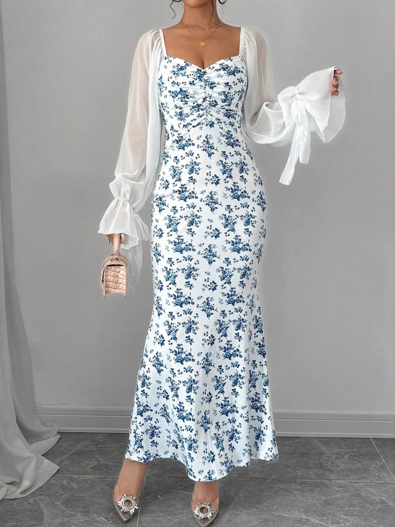 Woman wearing a floral dress with sheer sleeves against a gray background