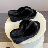 Pair of black fluffy slippers on a white stool against a neutral background