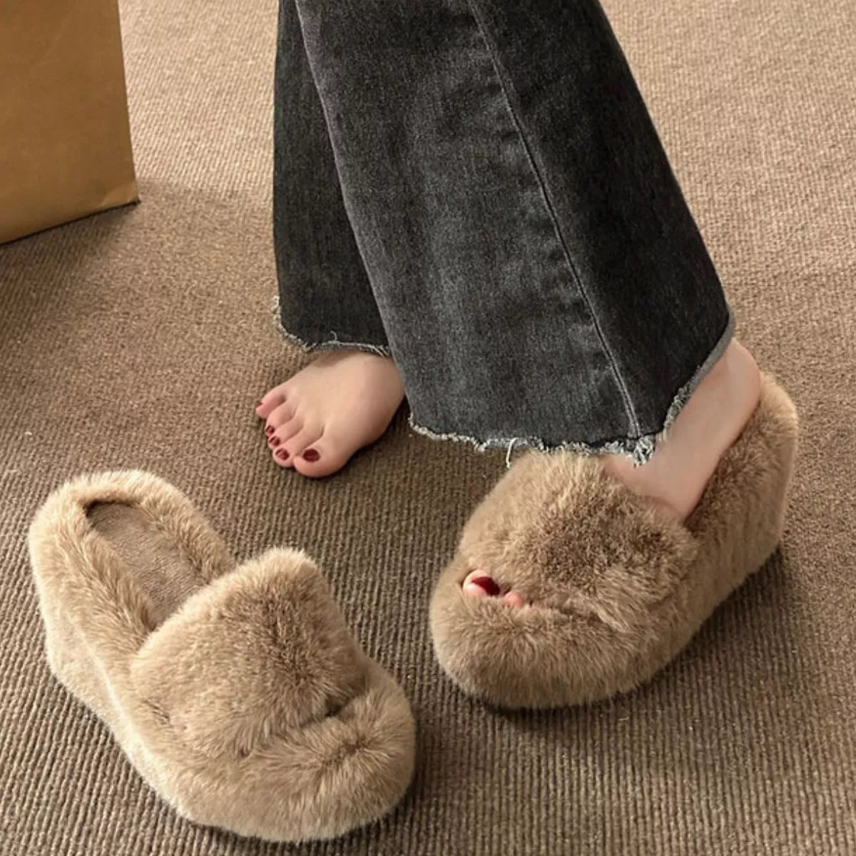 Beige fluffy slippers worn by a person on a carpeted floor.