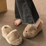 Beige fluffy slippers worn by a person on a carpeted floor.