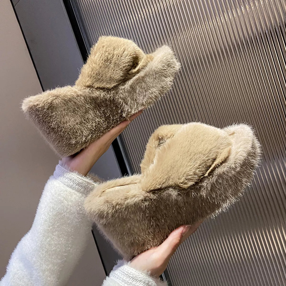 Pair of fluffy slippers held by a person wearing a white robe.