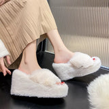 White fluffy slippers worn by a person sitting on a black surface.