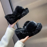 Black fluffy slippers held by a person wearing a white fuzzy sweater.