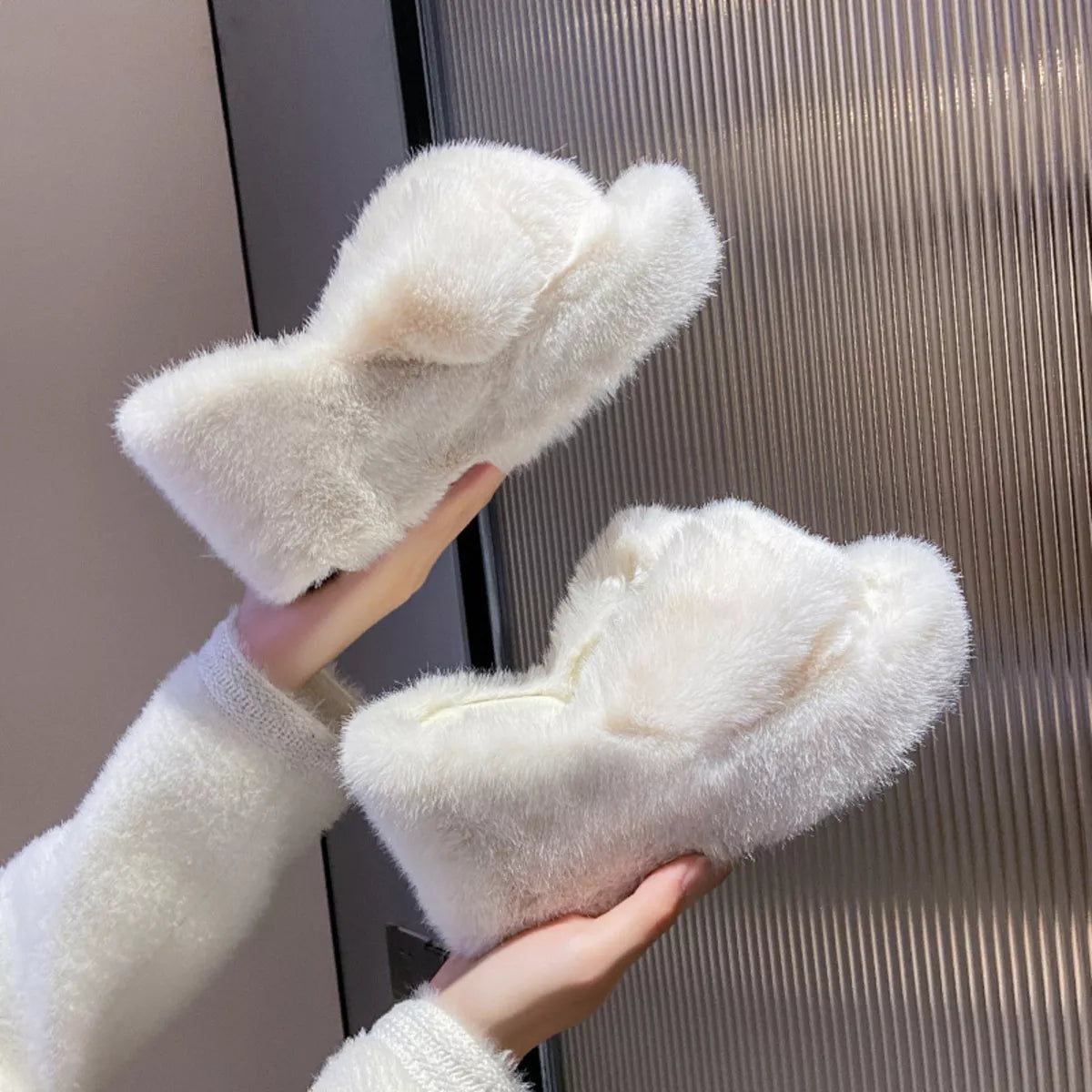 White fluffy slippers held by a hand against a neutral background