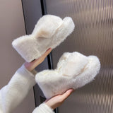 White fluffy slippers held by a hand against a neutral background
