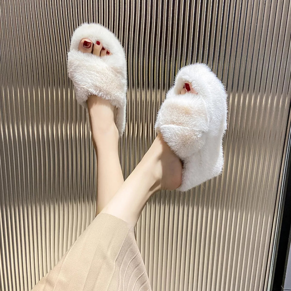 White fluffy slippers worn by a person on a textured floor.