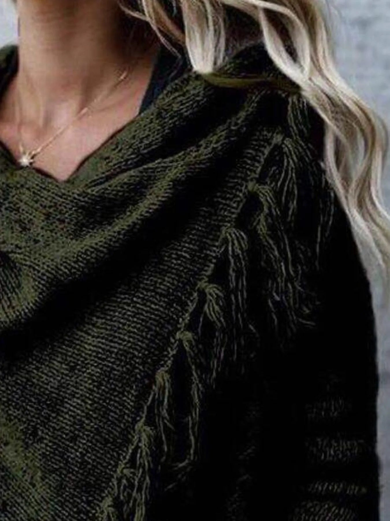 Woman wearing an army green fringe long sleeve wrap cardigan with an asymmetrical draped front over a white top and jeans.