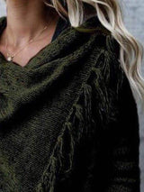 Woman wearing an army green fringe long sleeve wrap cardigan with an asymmetrical draped front over a white top and jeans.