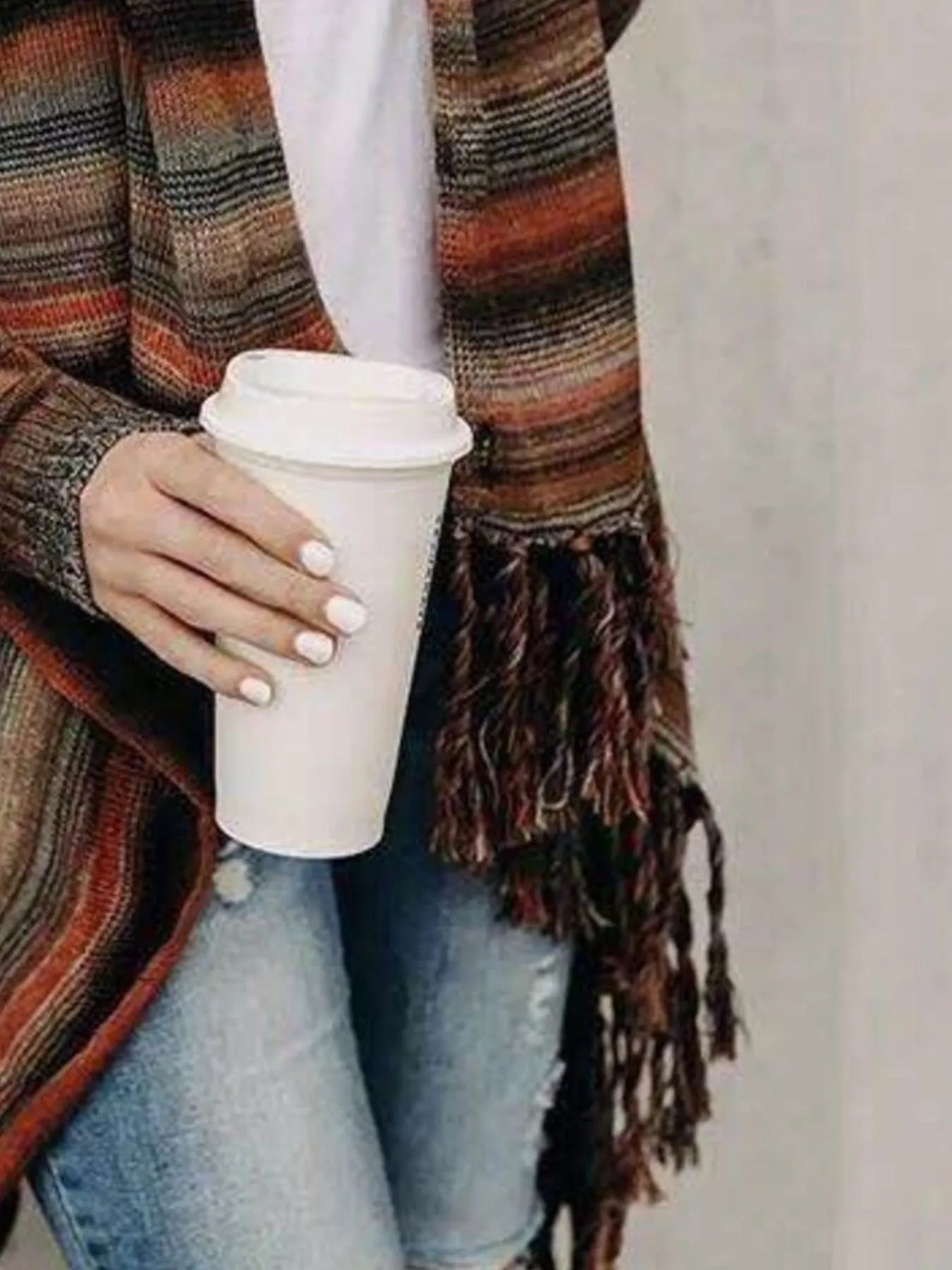 Woman wearing an orange stripe fringe long sleeve wrap cardigan with an asymmetrical draped front over a white top and jeans.