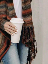Woman wearing an orange stripe fringe long sleeve wrap cardigan with an asymmetrical draped front over a white top and jeans.