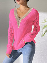 Woman wearing a fuchsia pink V-neck hollow knit sweater with contrasting neckline, openwork long sleeves, and blue jeans.