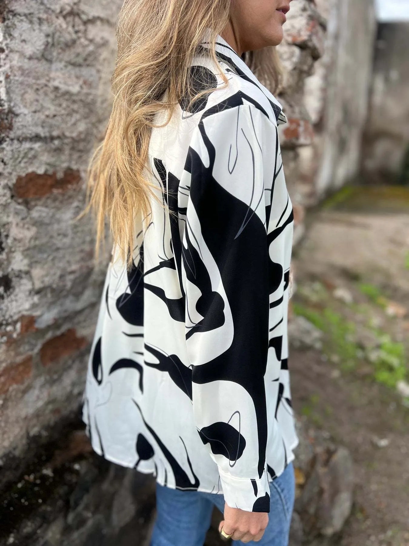 Person wearing a black and white abstract patterned shirt against a stone wall.