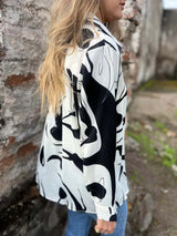 Person wearing a black and white abstract patterned shirt against a stone wall.