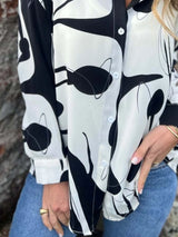 Person wearing a black and white patterned shirt with blue jeans.
