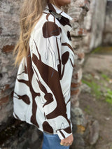 Person wearing a brown and white patterned shirt against a rustic stone wall showcasing the side of the shirt.
