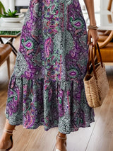 Woman wearing a purple bohemian paisley print midi dress with three-quarter sleeves and ruffled hem.