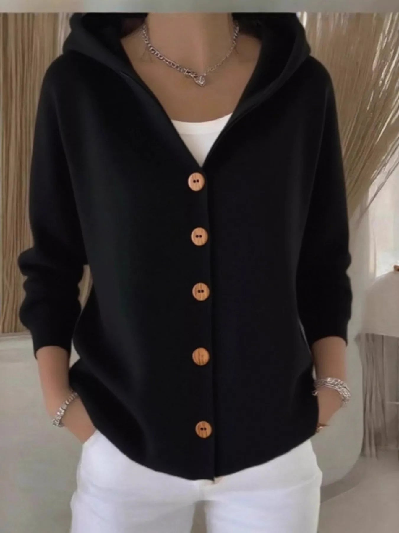 Women's black button-up knit cardigan with hood and front pockets, long sleeve lightweight sweater styled with white pants, available in sizes Small–5XL.