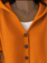 Women's orange button-up knit cardigan with hood and front pockets, long sleeve lightweight sweater styled with white pants, available in sizes Small–5XL.