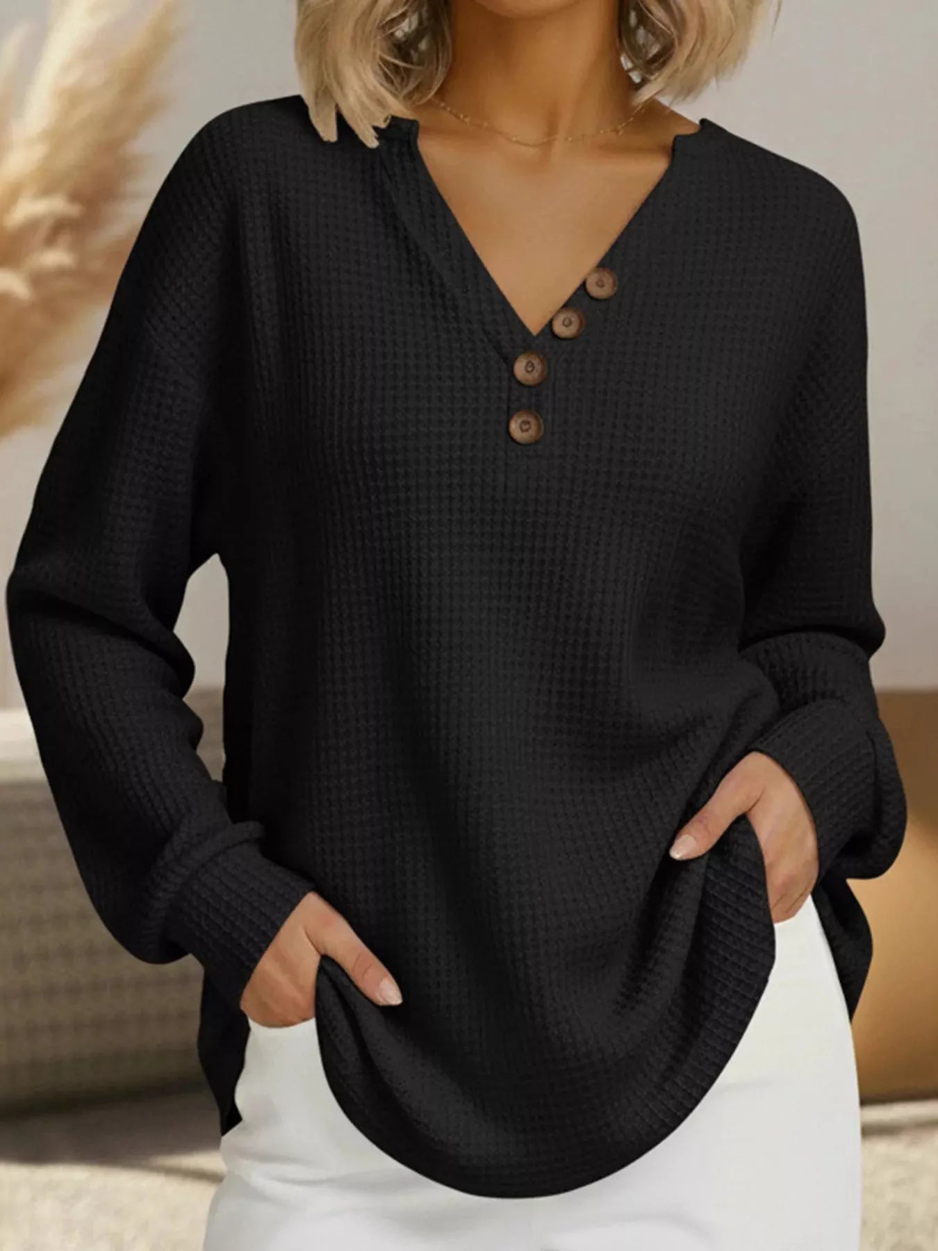 Person wearing a black textured long-sleeve top with buttons, standing indoors.
