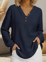 Navy blue textured sweater with brown buttons worn by a person indoors.