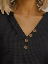 Close-up of a black textured top with wooden buttons worn by a person with blonde hair.
