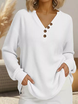 White ribbed sweater with brown buttons worn by a person, sitting on a couch.