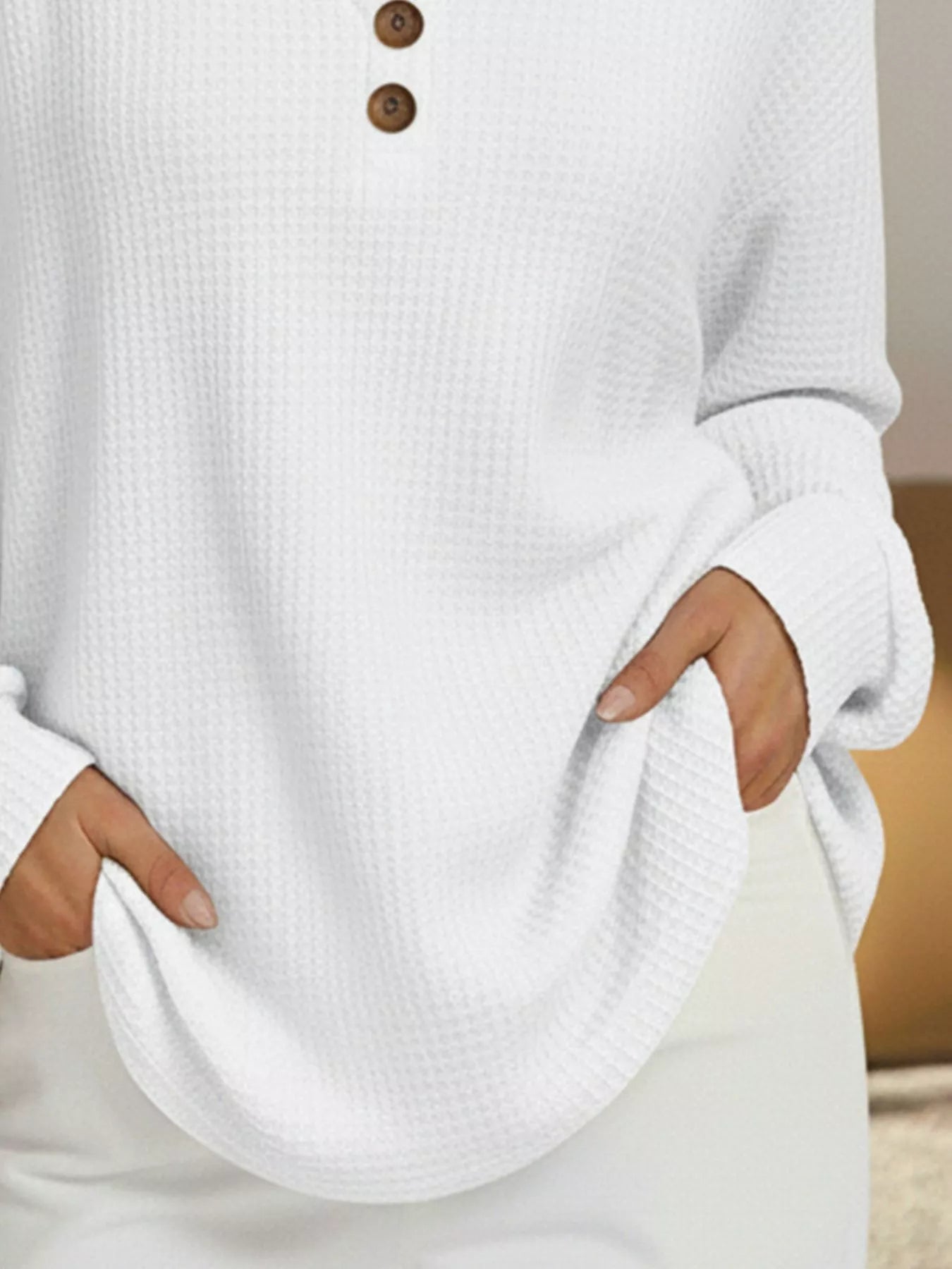 White sweater with brown buttons worn by a person, blurred background