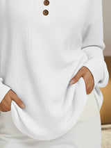 White sweater with brown buttons worn by a person, blurred background