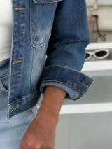 Woman wearing a dark blue cropped denim jacket over a white top with light-wash jeans and a structured handbag, styled for a chic fall outfit.