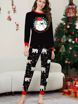 Mom wearing matching black Christmas pajamas with polar bear print, colorful holiday lights and red trim beside a Christmas tree.