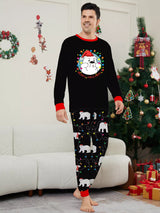 Dad wearing matching black Christmas pajamas with polar bear print, colorful holiday lights and red trim beside a Christmas tree.