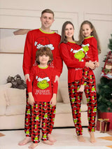Family of four wearing matching red Grinch-themed Christmas pajama tops and red and black plaid printed pants beside a Christmas tree.