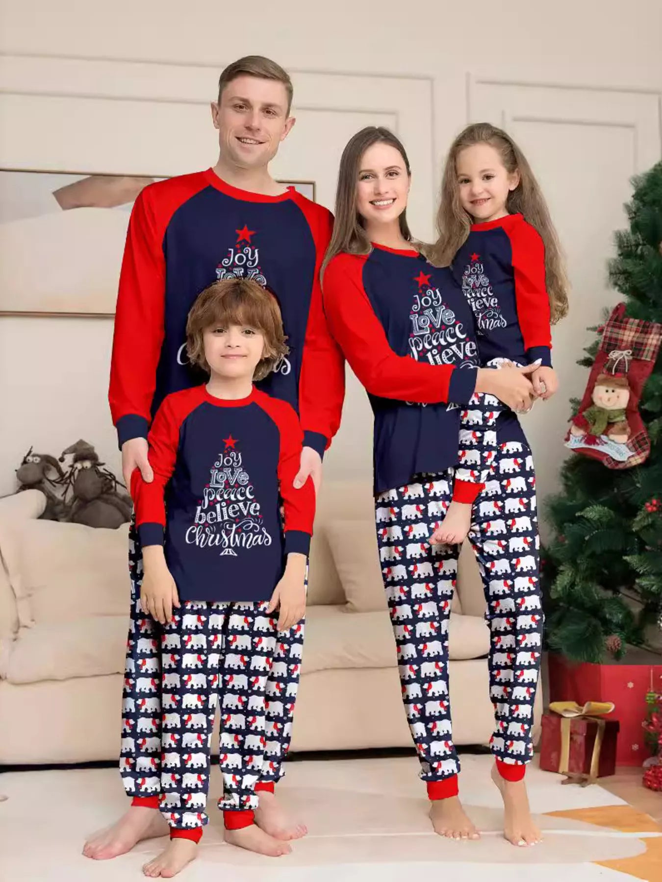 Family of four wearing matching Christmas pajamas with navy tops, red raglan sleeves, festive Christmas tree lettering, and coordinating printed pants.