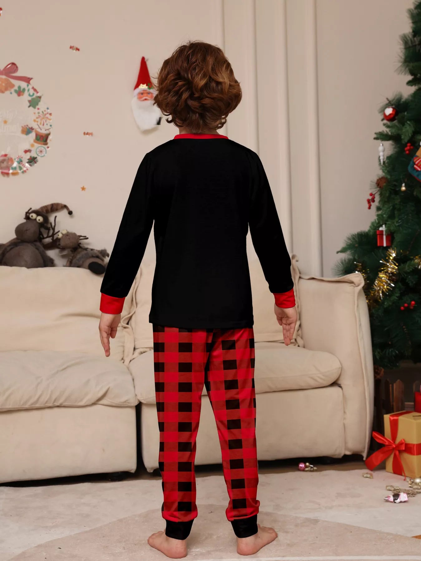 Boy wearing matching Christmas Crew graphic pajama sets with black long-sleeve tops and red buffalo plaid pants.
