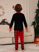 Boy wearing matching Christmas Crew graphic pajama sets with black long-sleeve tops and red buffalo plaid pants.