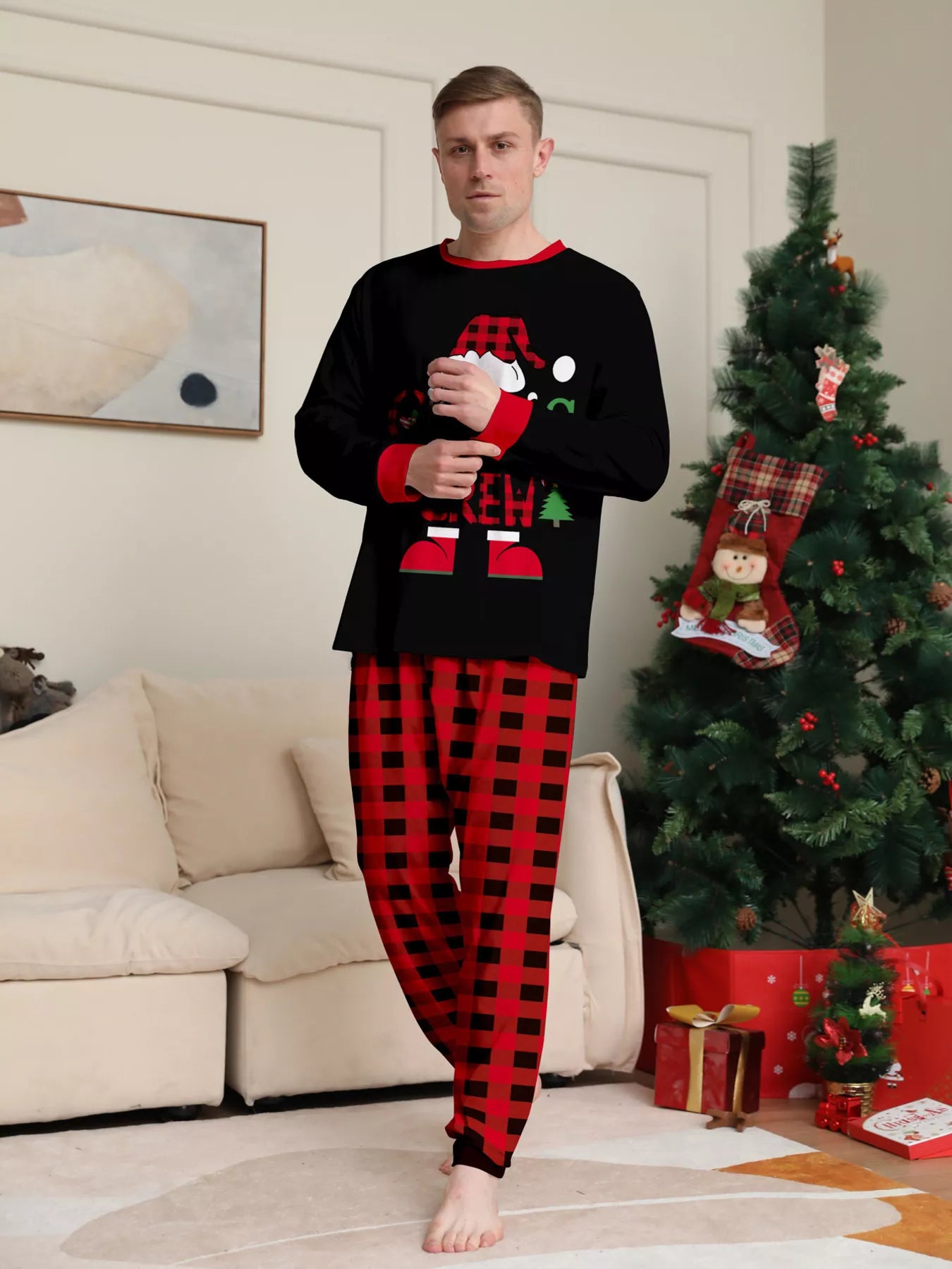 Dad modeling matching Christmas Crew pajama sets with festive black graphic tops and red and black plaid pants.