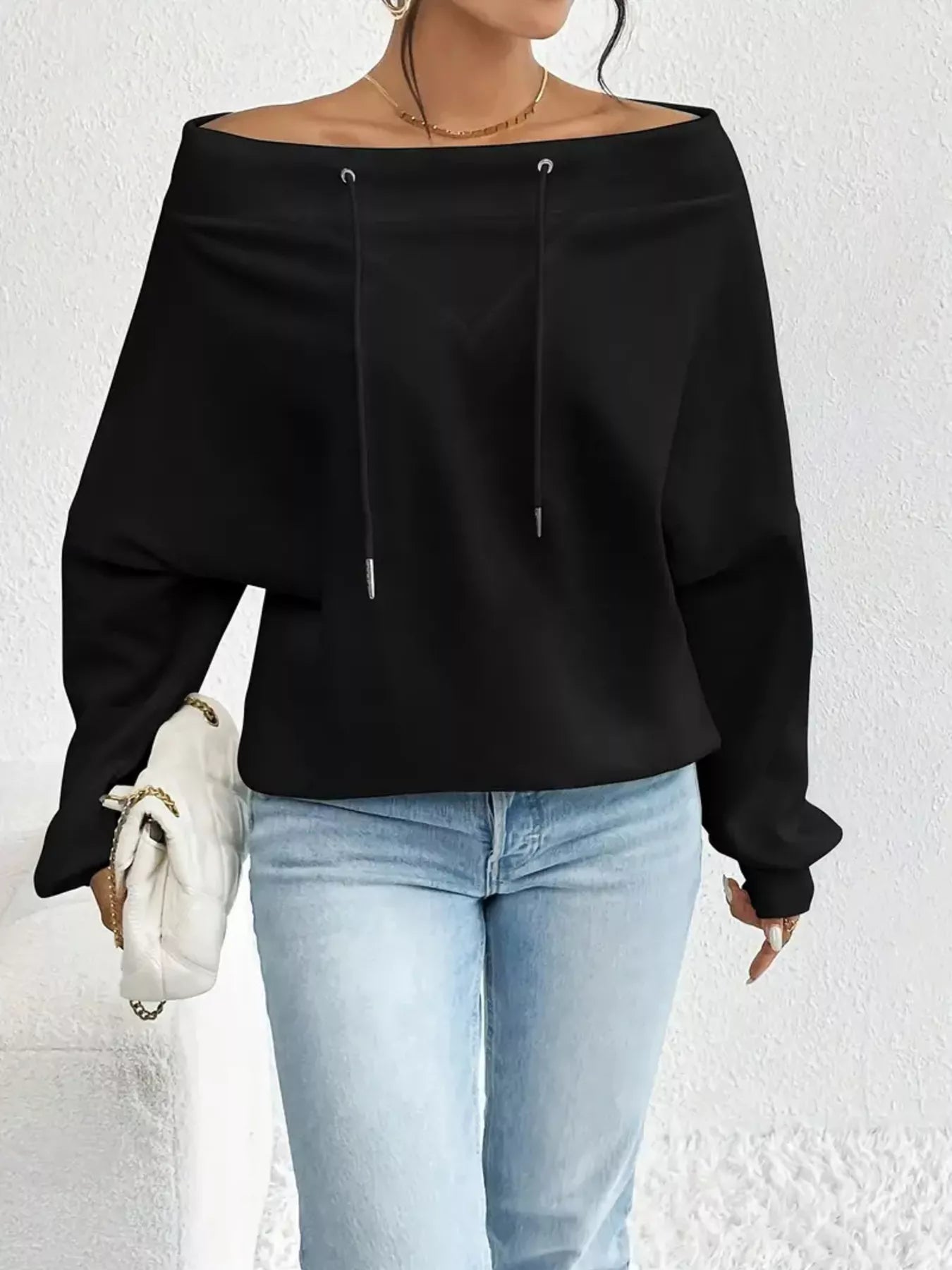 Person wearing a black off-shoulder top and light blue jeans against a white background