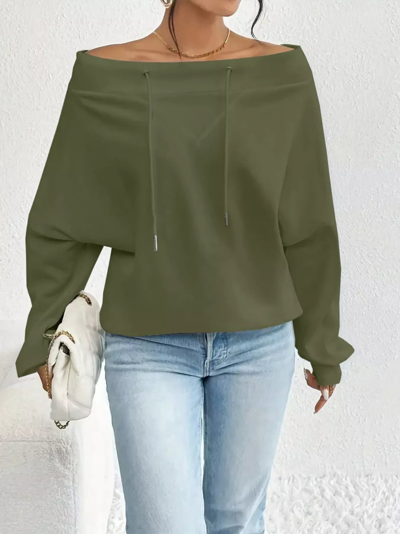 Person wearing an olive green off-shoulder top and light blue jeans against a white background