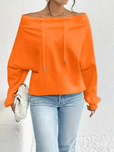 Person wearing an orange red off-shoulder top and light blue jeans against a white background