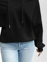 Person wearing a black hoodie and light blue jeans against a white background